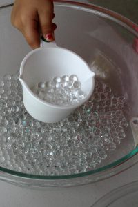 Introducing water beads by scooping with a measuring cup from Happilyevermom